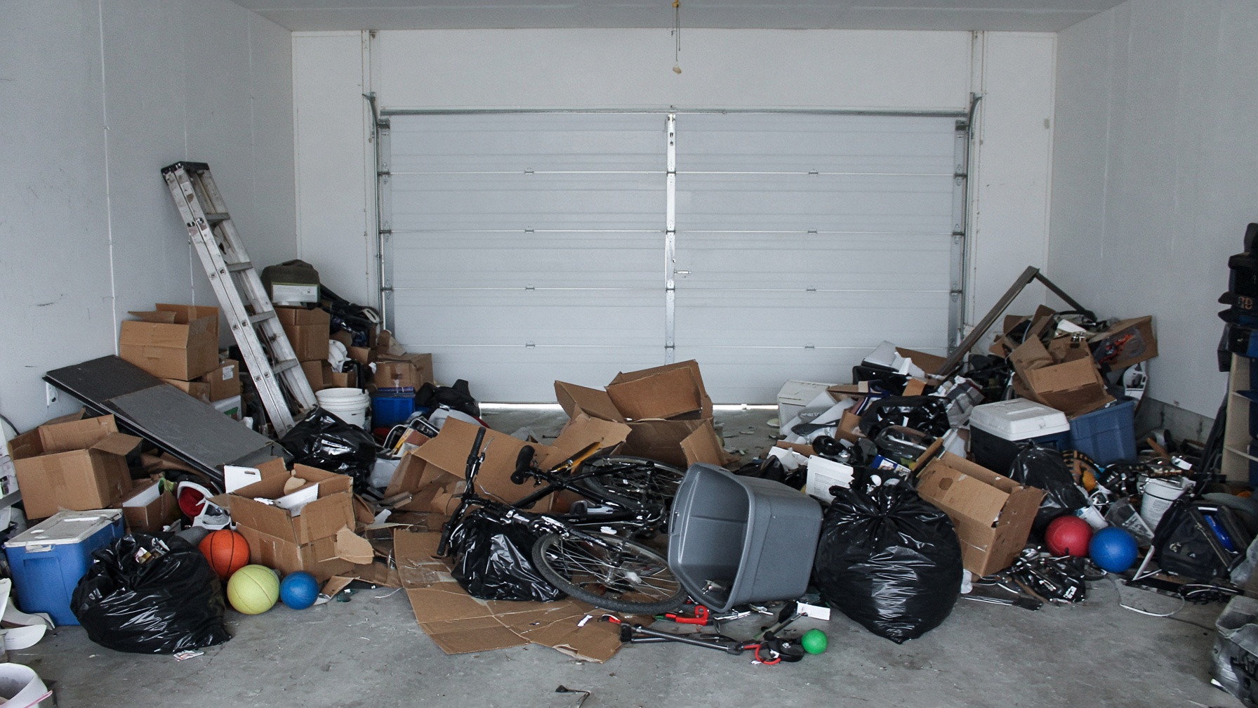 Chaotic two-car garage with boxes, bags, and gear piled across the floor